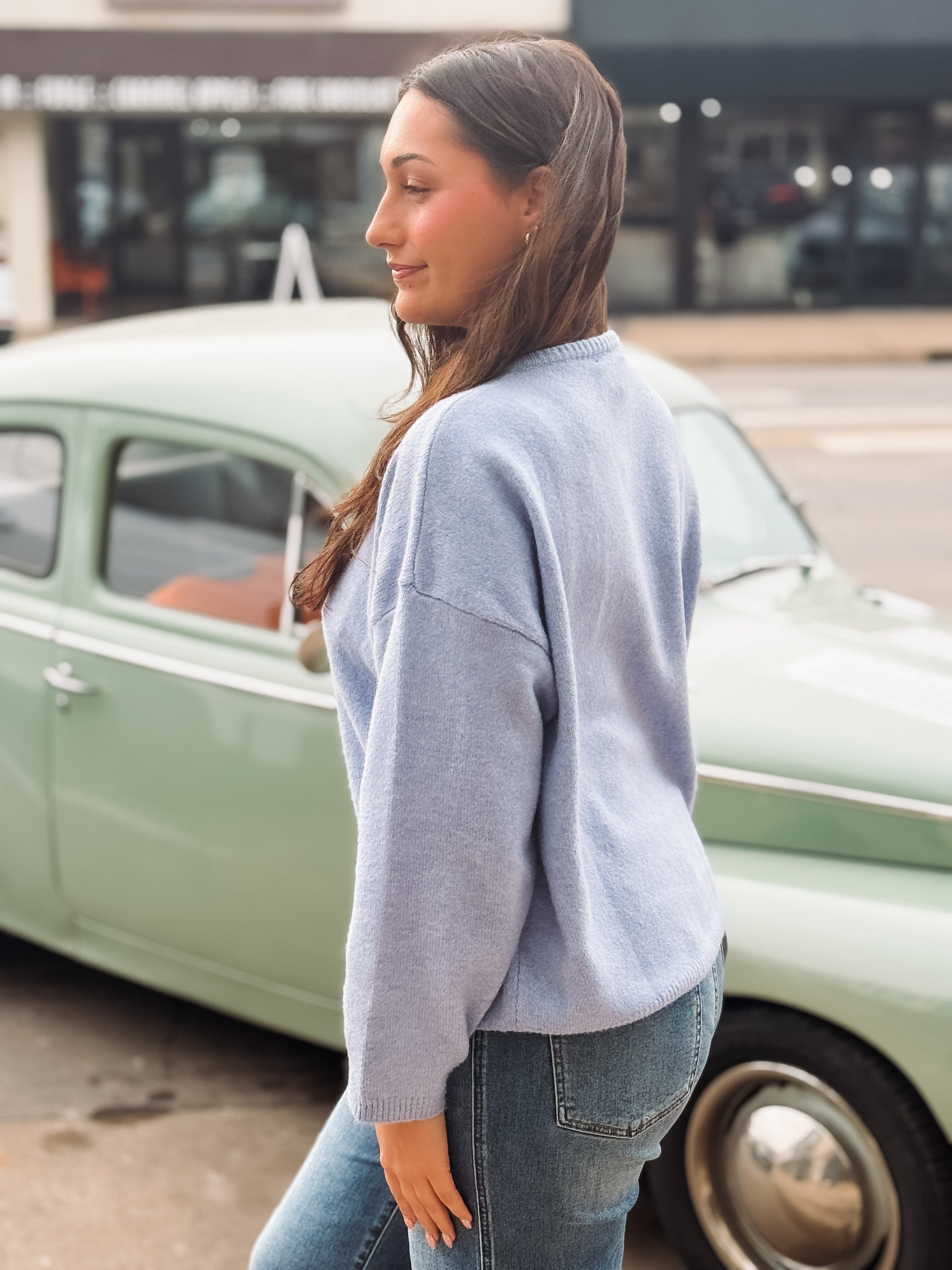 Woman in a light blue sweater and jeans standing next to a vintage car.