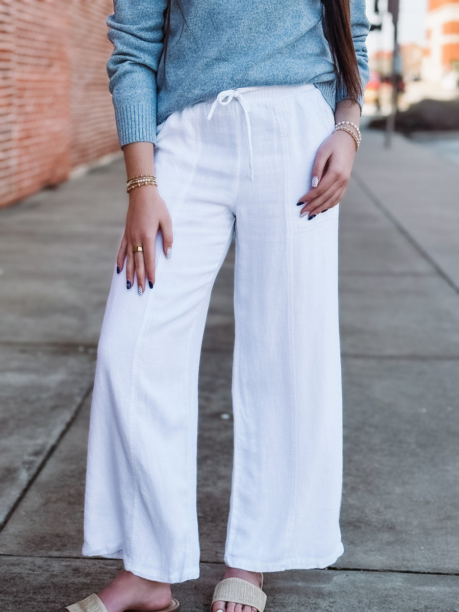 Person wearing white wide-leg pants and a blue sweater on a sidewalk.