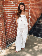 Strapless ecru matching pant  set featuring a flowy tube top with an elastic neckline and wide leg pants with an elastic drawstring waistband, pockets, and a soft light brown polka dot print.