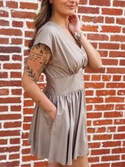 Taupe brown colored short sleeve mini dress. Features a full button front, a cinched waist and a V neckline. 