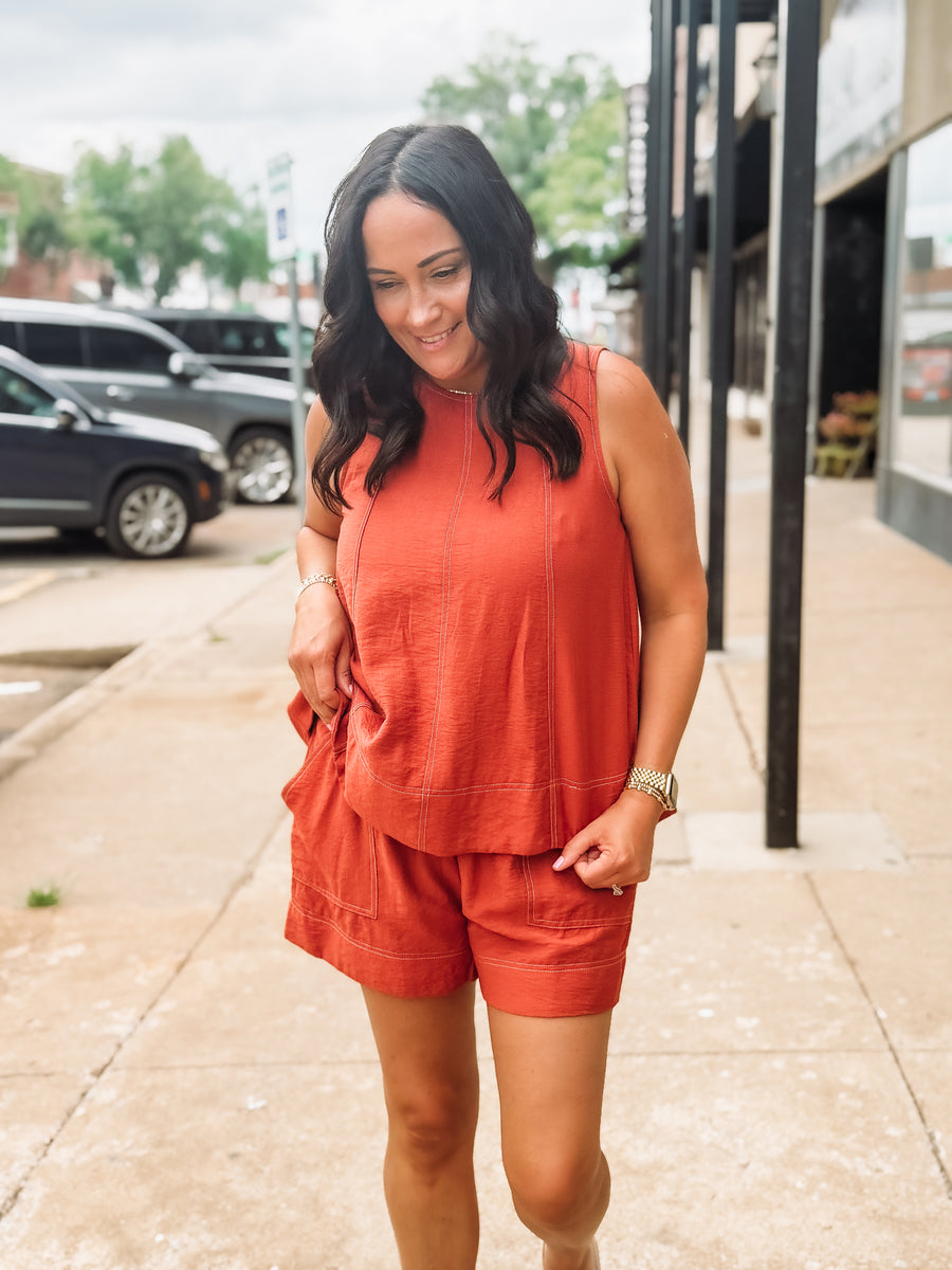 Woman wearing an orange outfit standing on a sidewalk with cars and buildings in the background