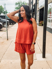 Woman wearing an orange sleeveless top and shorts on a sidewalk.