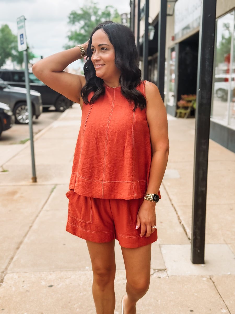 Woman wearing an orange sleeveless top and shorts on a sidewalk.