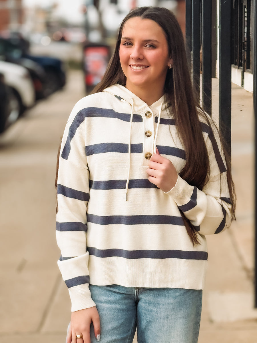 Woman wearing a striped hoodie and jeans standing on a street.