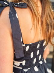 Black and white polka dot maxi dress with spaghetti straps, a tiered silhouette, and faux gold button details.
