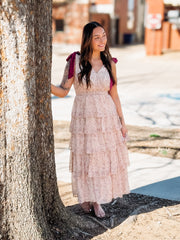 Woman in a floral dress standing next to a tree on a sunny day.