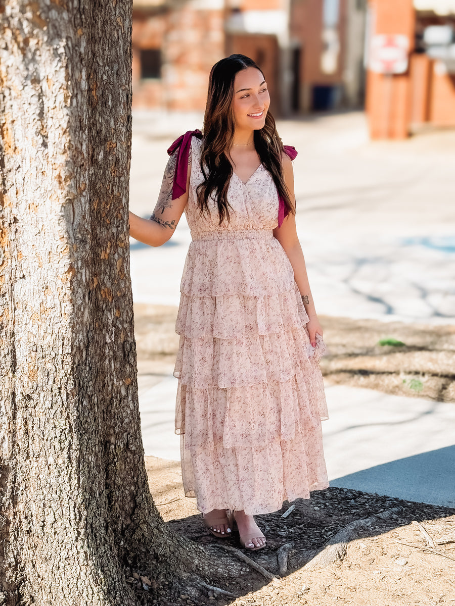 Woman in a floral dress standing next to a tree on a sunny day.