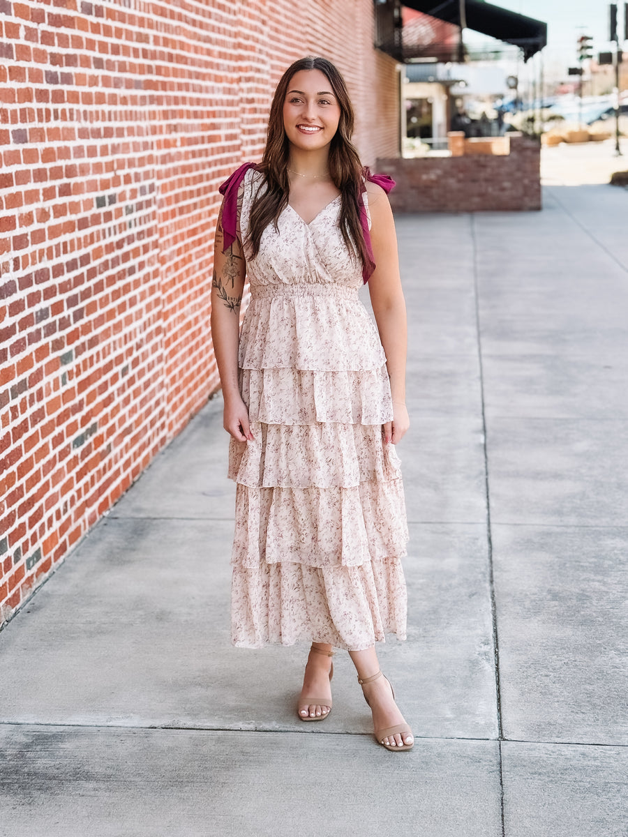 Woman in a floral dress standing on a sidewalk next to a brick wall.