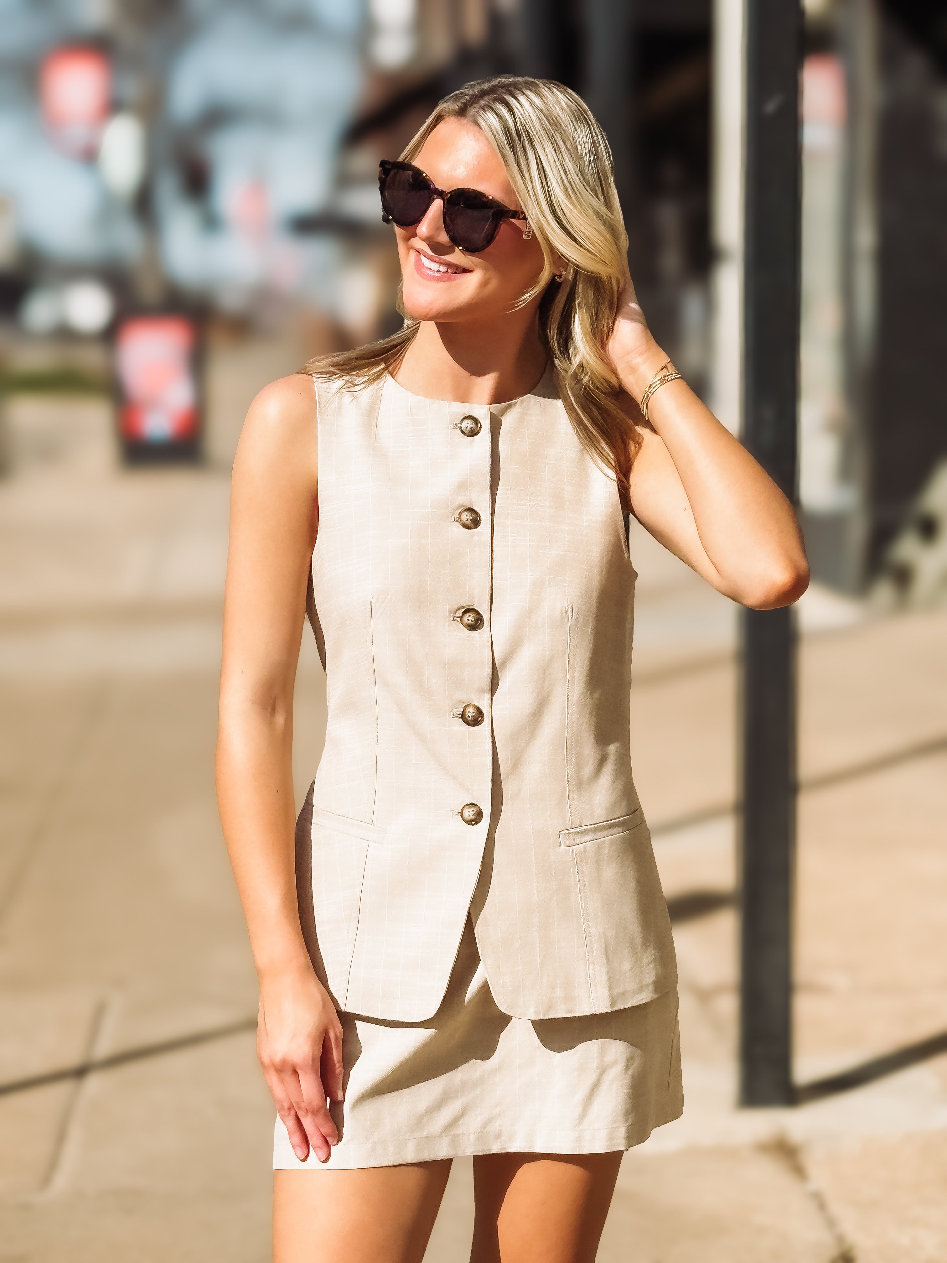 Woman wearing a beige sleeveless top and skirt on a city street.