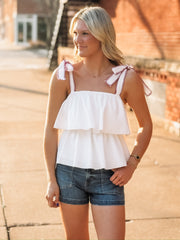 White ruffled tank top with bow tie shoulder straps that have a magenta detail and a flowy layered design. 