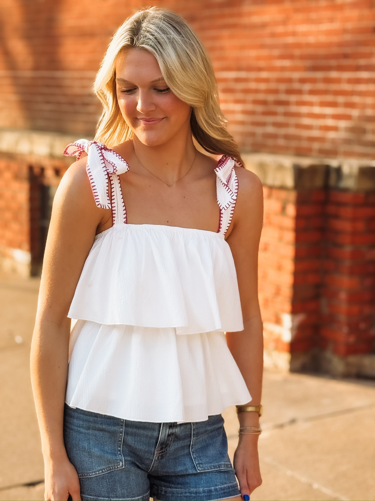 White ruffled tank top with bow tie shoulder straps that have a magenta detail and a flowy layered design. 