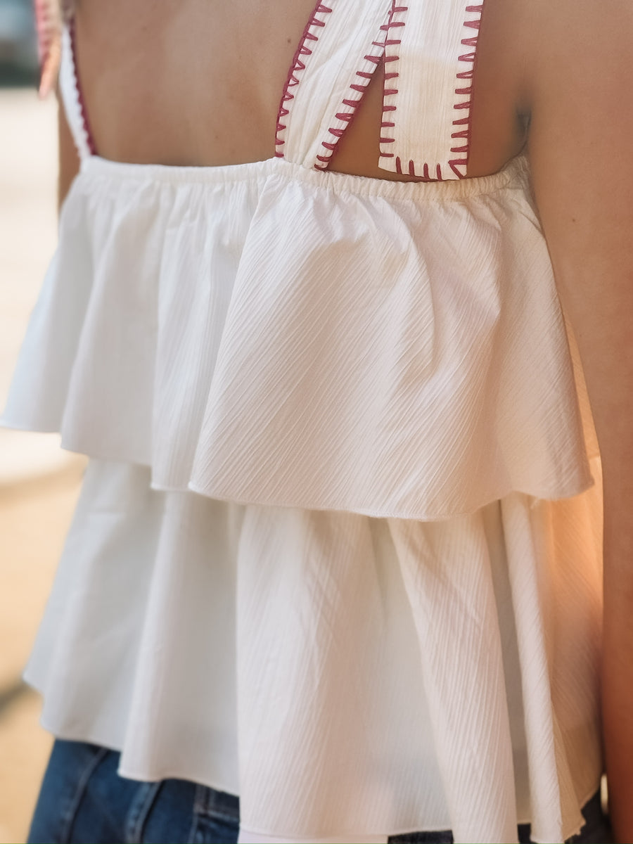 White ruffled tank top with bow tie shoulder straps that have a magenta detail and a flowy layered design. 