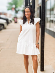Woman wearing a white dress standing on a sidewalk with blurred background