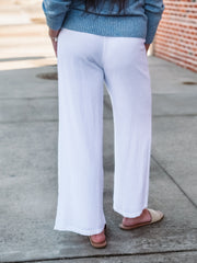 Person wearing white pants and a blue sweater on a sidewalk.