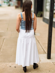 Woman wearing a white skirt with denim straps walking on a sidewalk.