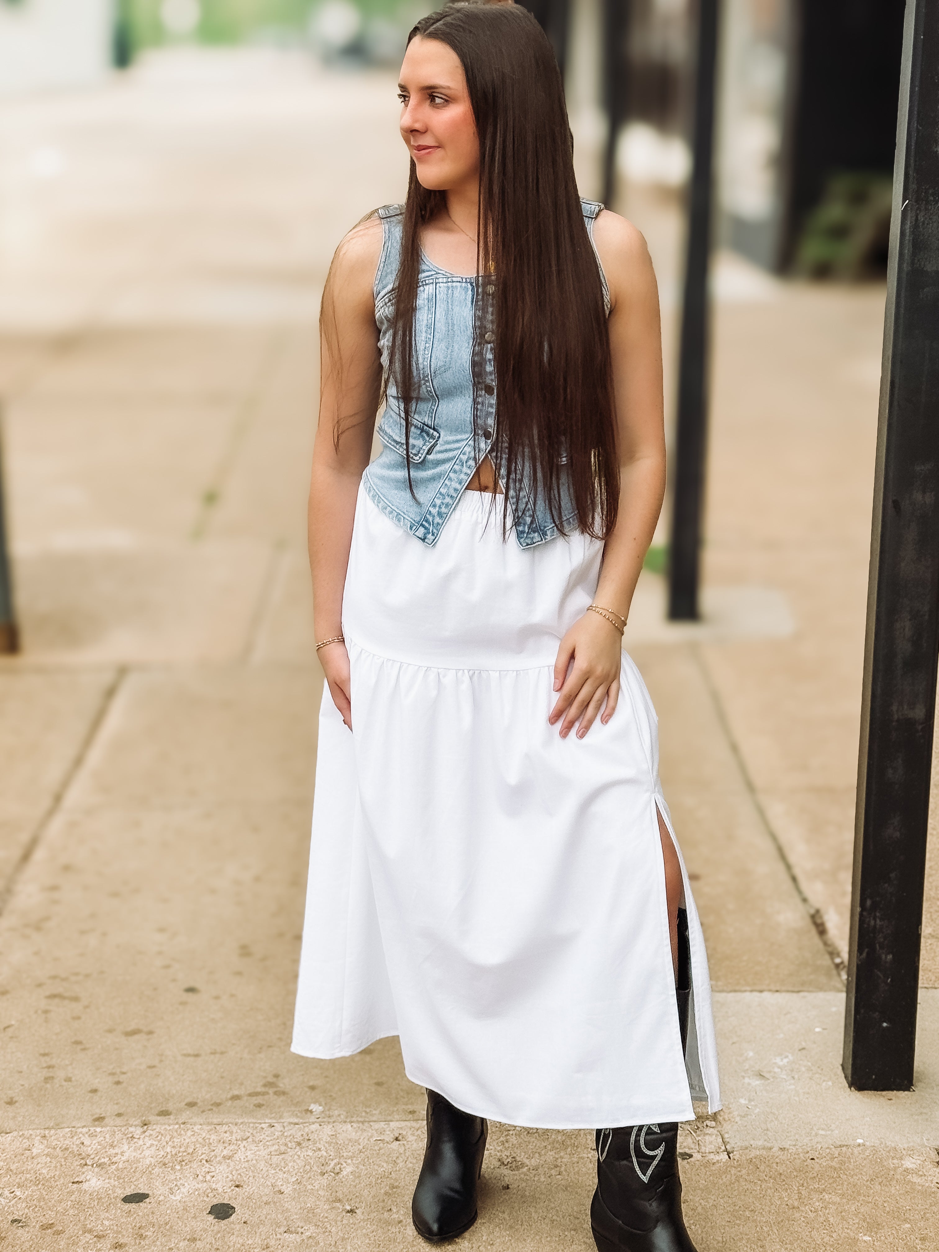 Woman wearing a denim top and white dress on a sidewalk.