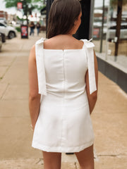 Woman wearing a white dress with bow straps on a city street.
