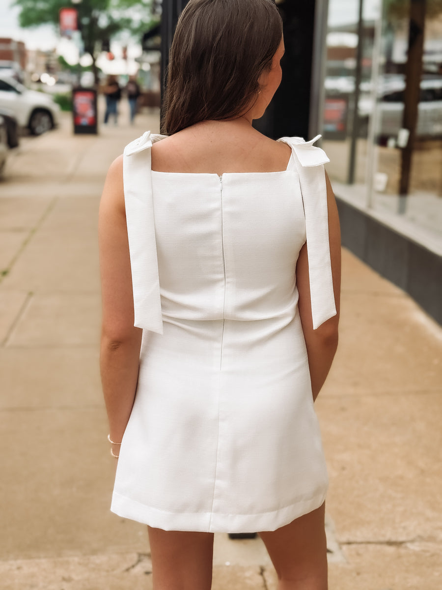 Woman wearing a white dress with bow straps on a city street.