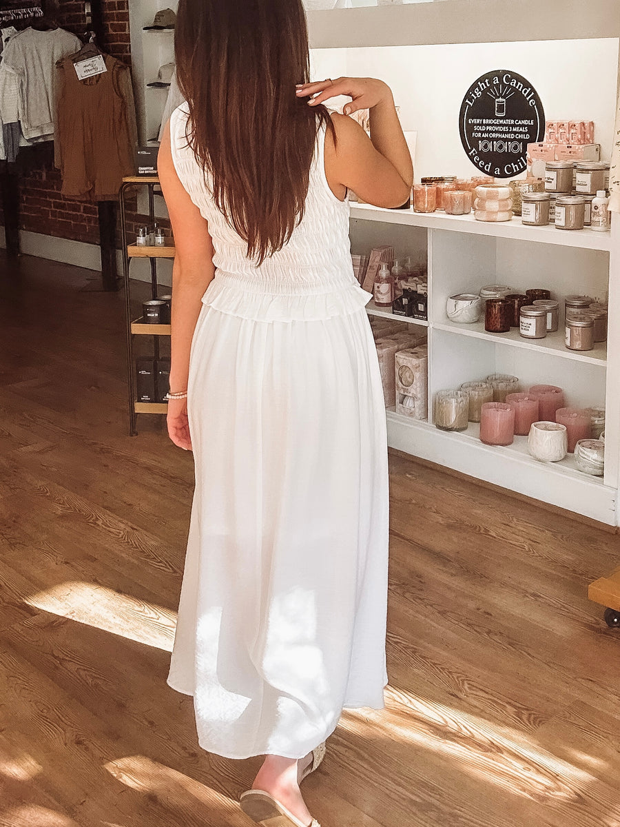 Woman in a white dress standing in a store with shelves of products.