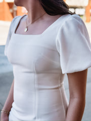 White mini dress featuring short puff sleeves, a flattering body-con silhouette, and a square neckline. Designed in a textured waffle knit for added detail and dimension.