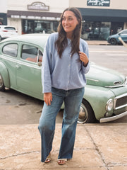 Woman in a blue shirt and jeans standing in front of a vintage car.