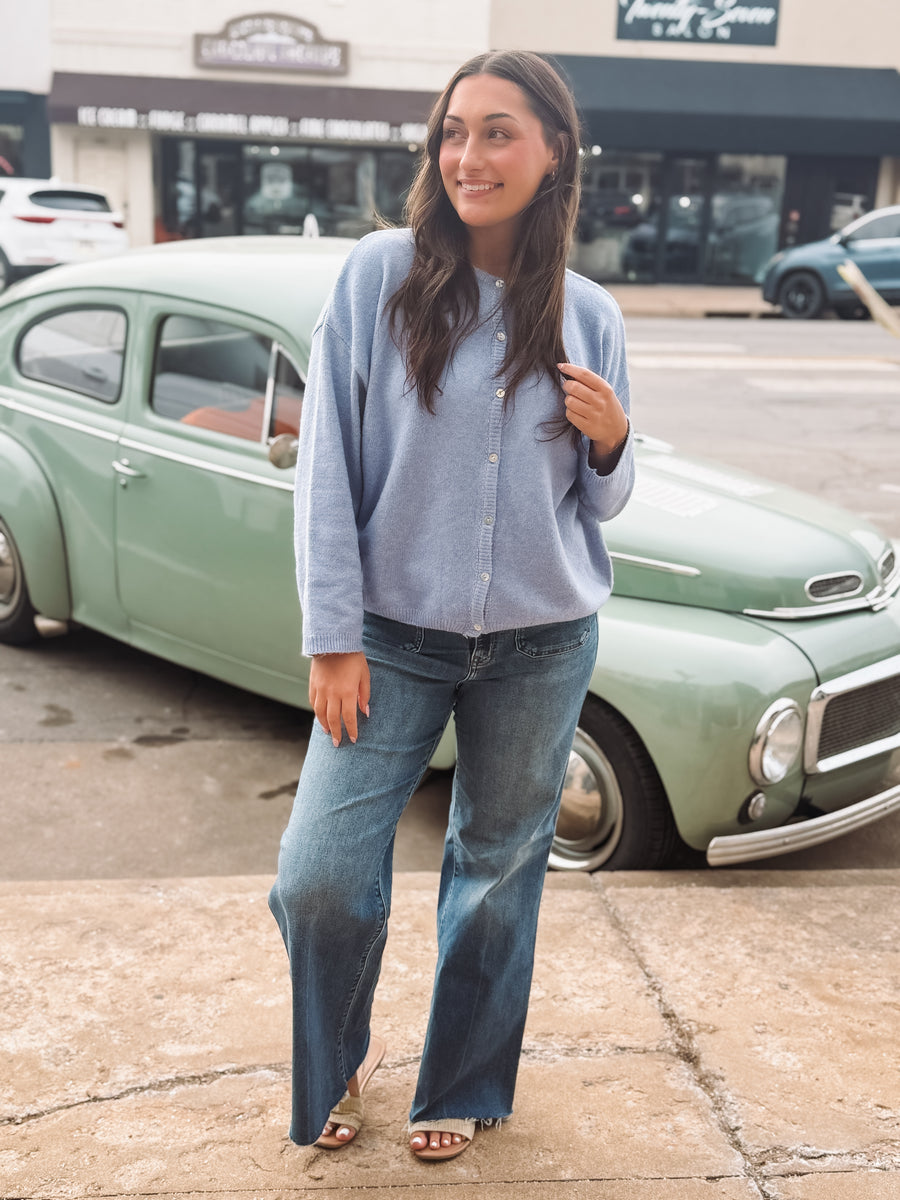 Woman in a blue shirt and jeans standing in front of a vintage car.