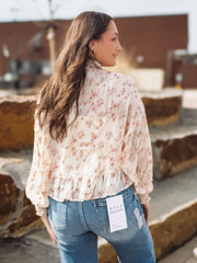 Woman wearing a floral blouse and blue jeans with a brand tag, standing outdoors.