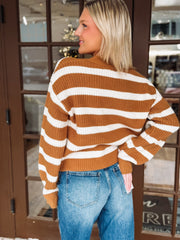 Woman wearing a brown and white striped sweater and blue jeans indoors.