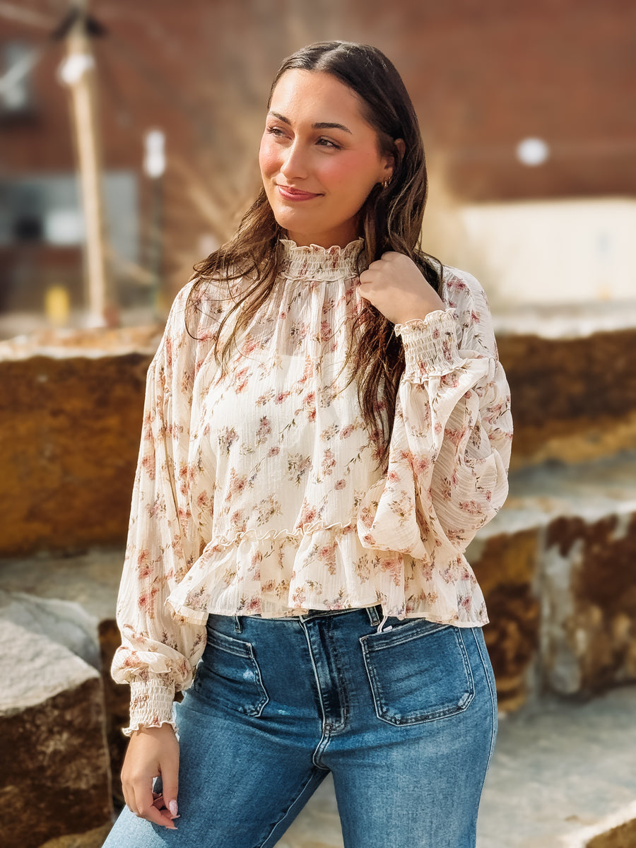 Woman wearing a floral blouse and blue jeans standing outdoors.