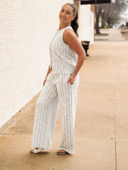 Sleeveless, textured two-piece outfit in a soft light blue and white woven fabric. The top features a round neckline, front button detailing, and a slightly relaxed, straight fit. The matching pants are high-waisted with a wide-leg silhouette