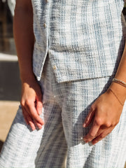 Sleeveless, textured two-piece outfit in a soft light blue and white woven fabric. The top features a round neckline, front button detailing, and a slightly relaxed, straight fit. The matching pants are high-waisted with a wide-leg silhouette