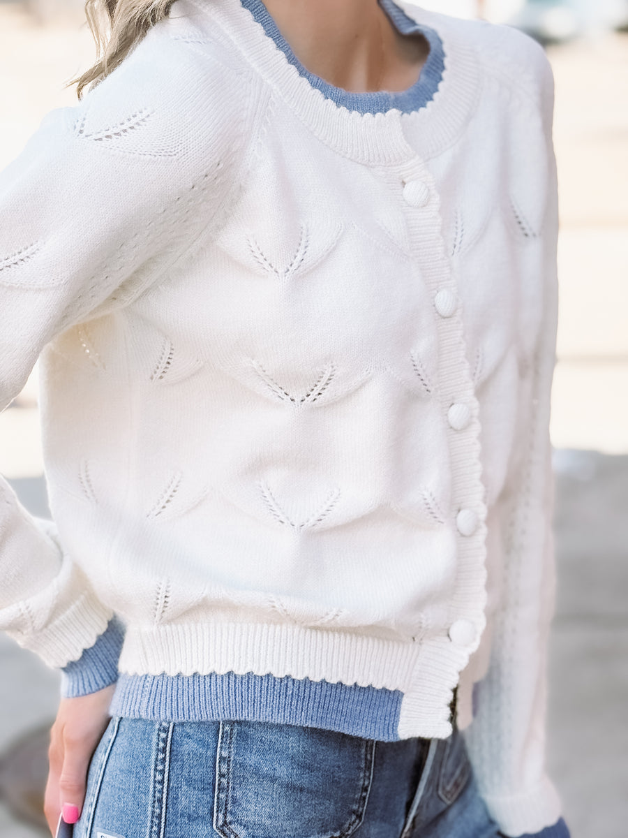 White sweater with blue trim worn by a person, blurred background