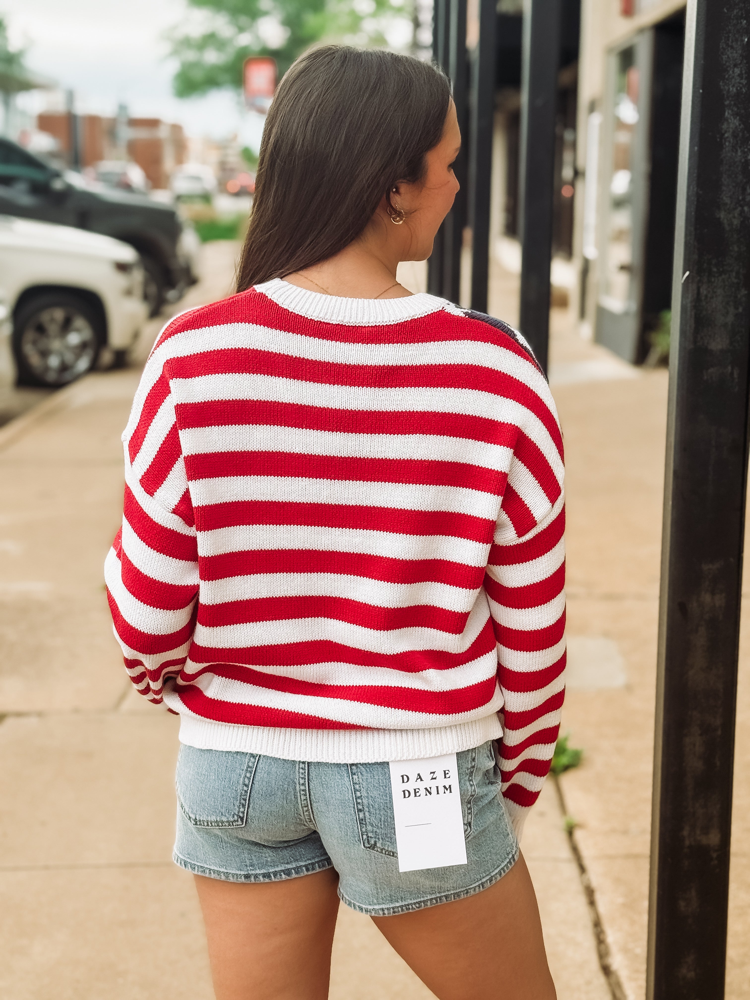 Woman wearing a red and white striped sweater and denim shorts on a sidewalk.