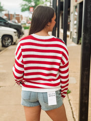 Woman wearing a red and white striped sweater and denim shorts on a sidewalk.
