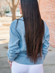 Person wearing a light blue sweater with long dark hair, standing outdoors.