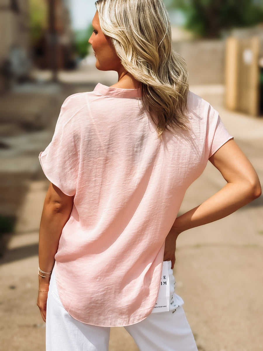 Woman wearing a light pink shirt and white pants outdoors