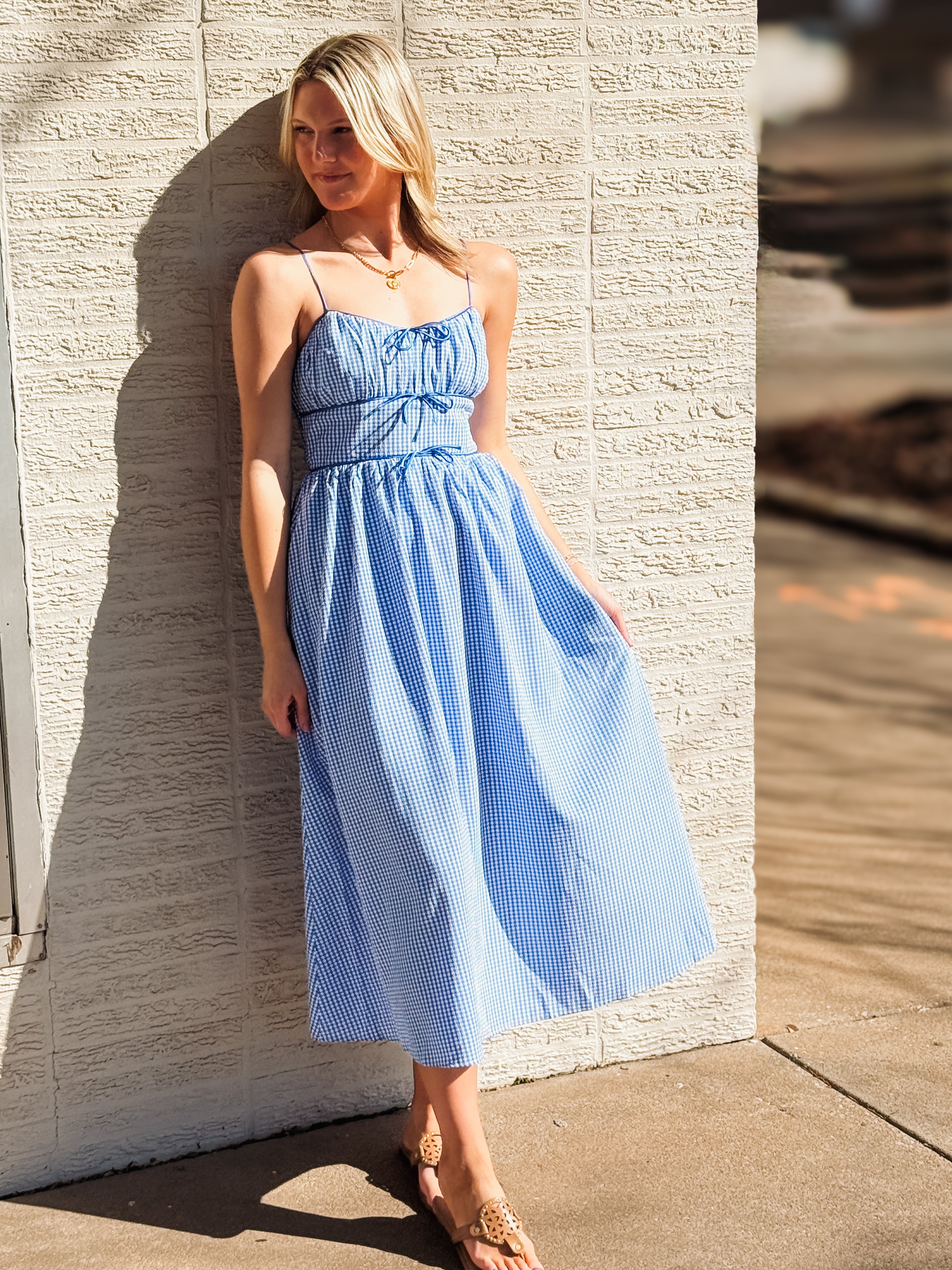 Woman in a blue dress standing against a textured wall.