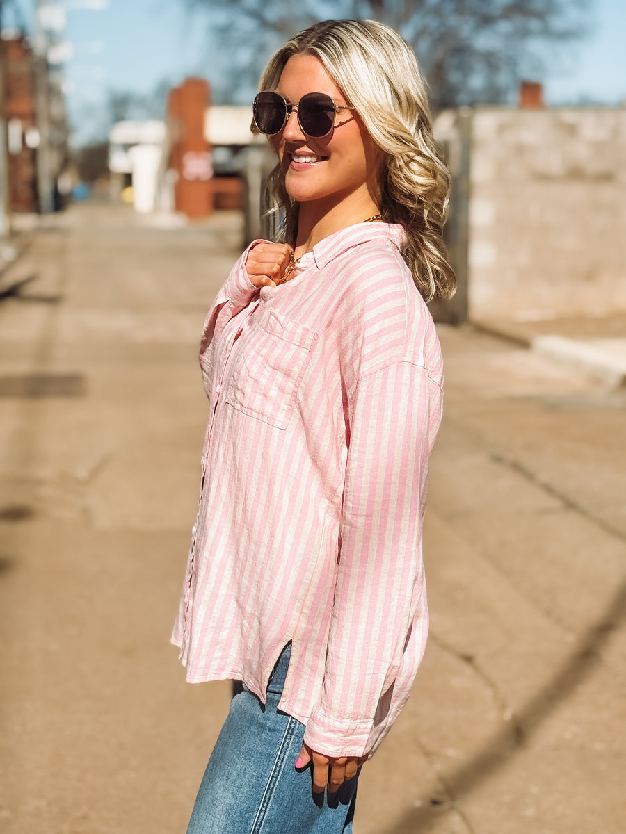 Woman wearing a pink striped shirt and sunglasses on a sunny day.