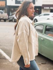 Woman wearing a beige jacket standing on a street with cars in the background