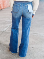 Person wearing blue flared jeans with a visible brand tag on a concrete surface.