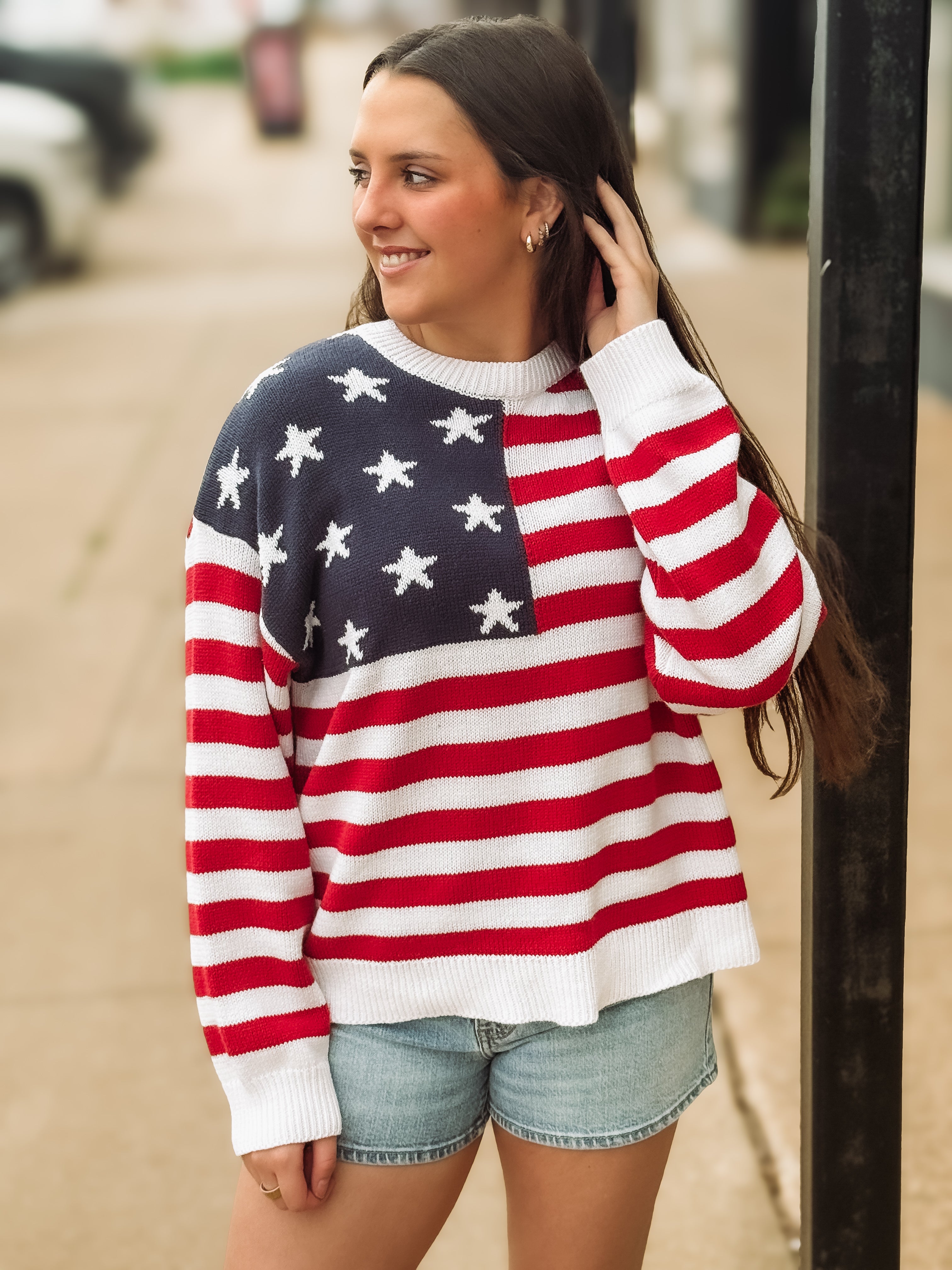 Woman wearing a red, white, and blue flag sweater on a street.
