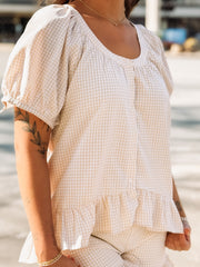 Person wearing a white checkered dress with ruffled sleeves and hem.