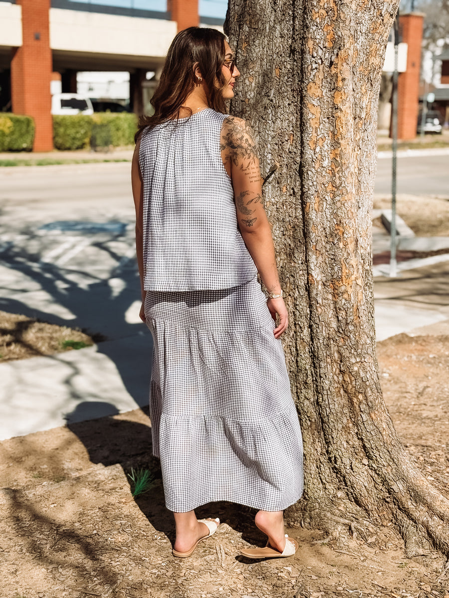 Woman in a long, light-colored dress standing next to a tree on a street.