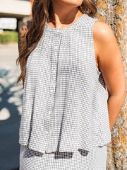 Woman wearing a black and white checkered sleeveless top against a blurred outdoor background.