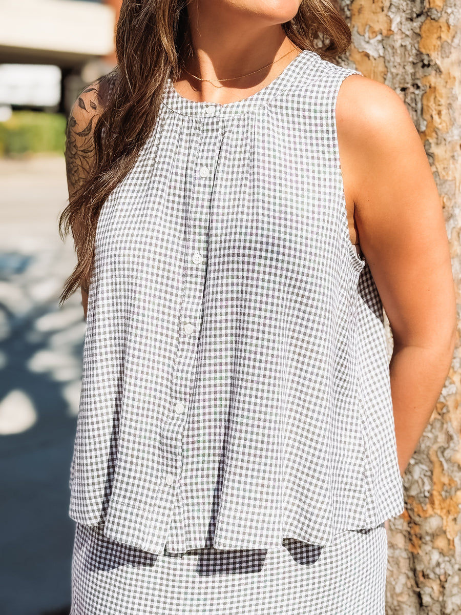 Woman wearing a black and white checkered sleeveless top against a blurred outdoor background.