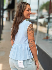 Woman wearing a light blue sleeveless top with a blurred outdoor background
