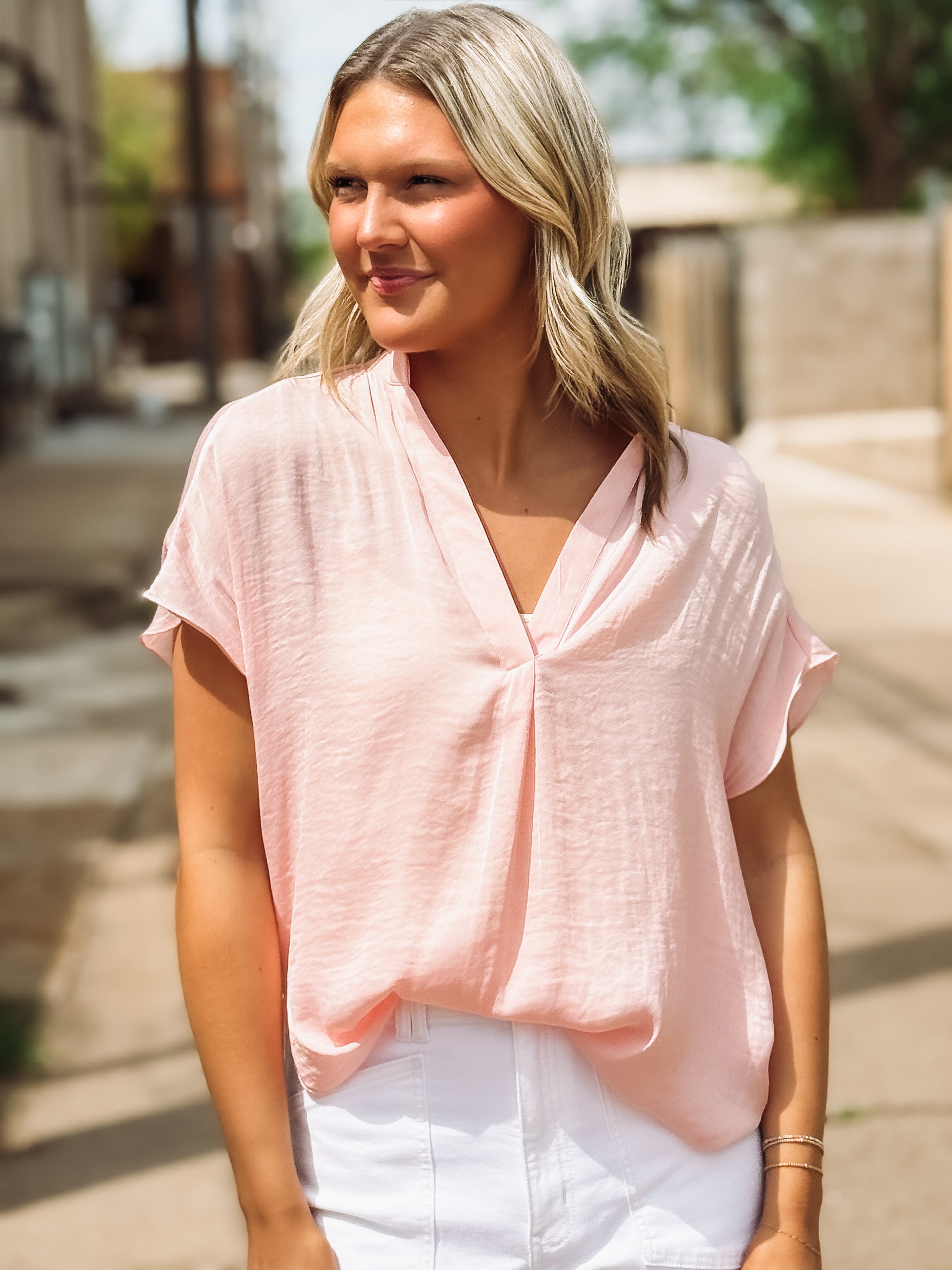 Woman wearing a light pink blouse and white pants outdoors.