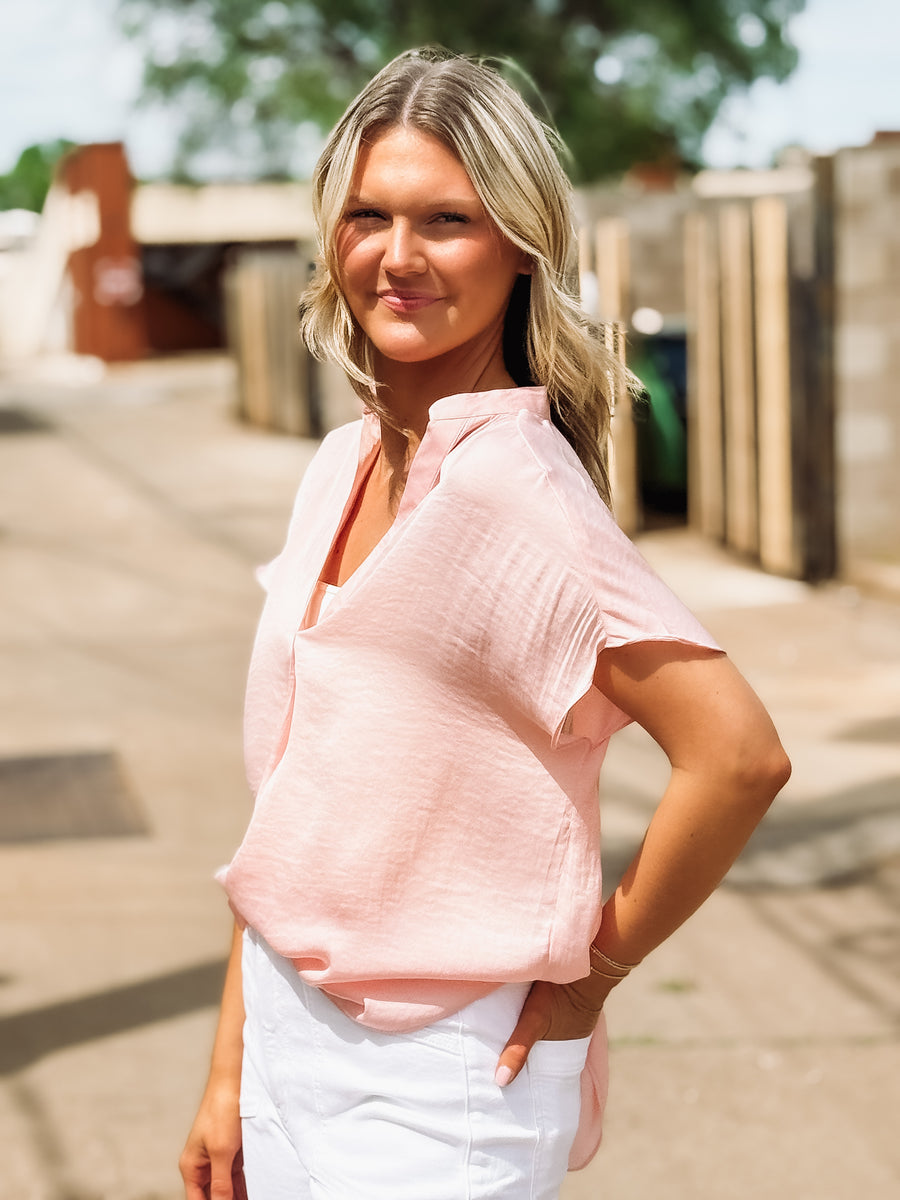 Woman wearing a pink blouse and white pants outdoors.