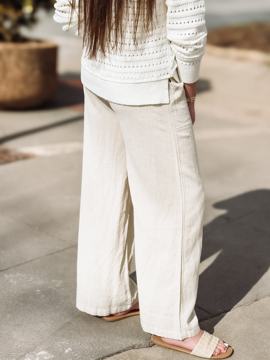 Person wearing a white crochet top and wide-leg pants on a concrete surface.