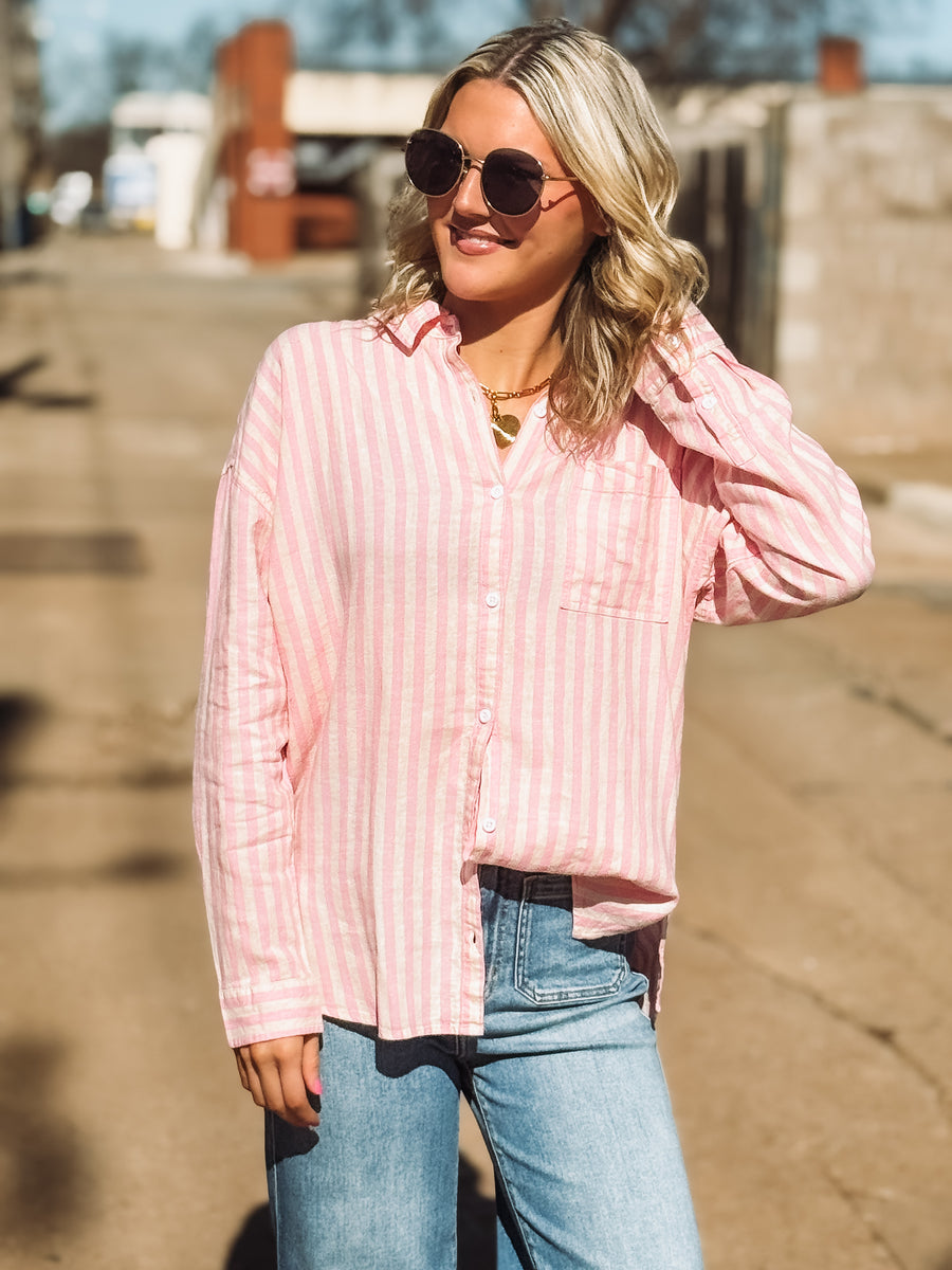Woman wearing a pink striped shirt and blue jeans outdoors.